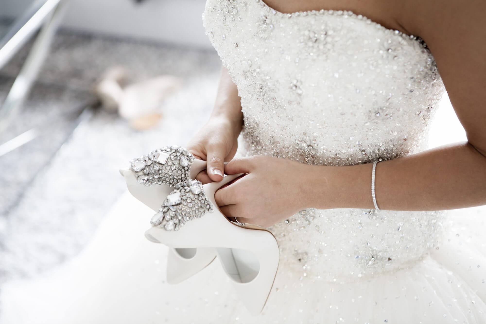 Stock photo of bride from the shoulders down wearing sparkly wedding dress and holding a pair of white sparkly high heels.