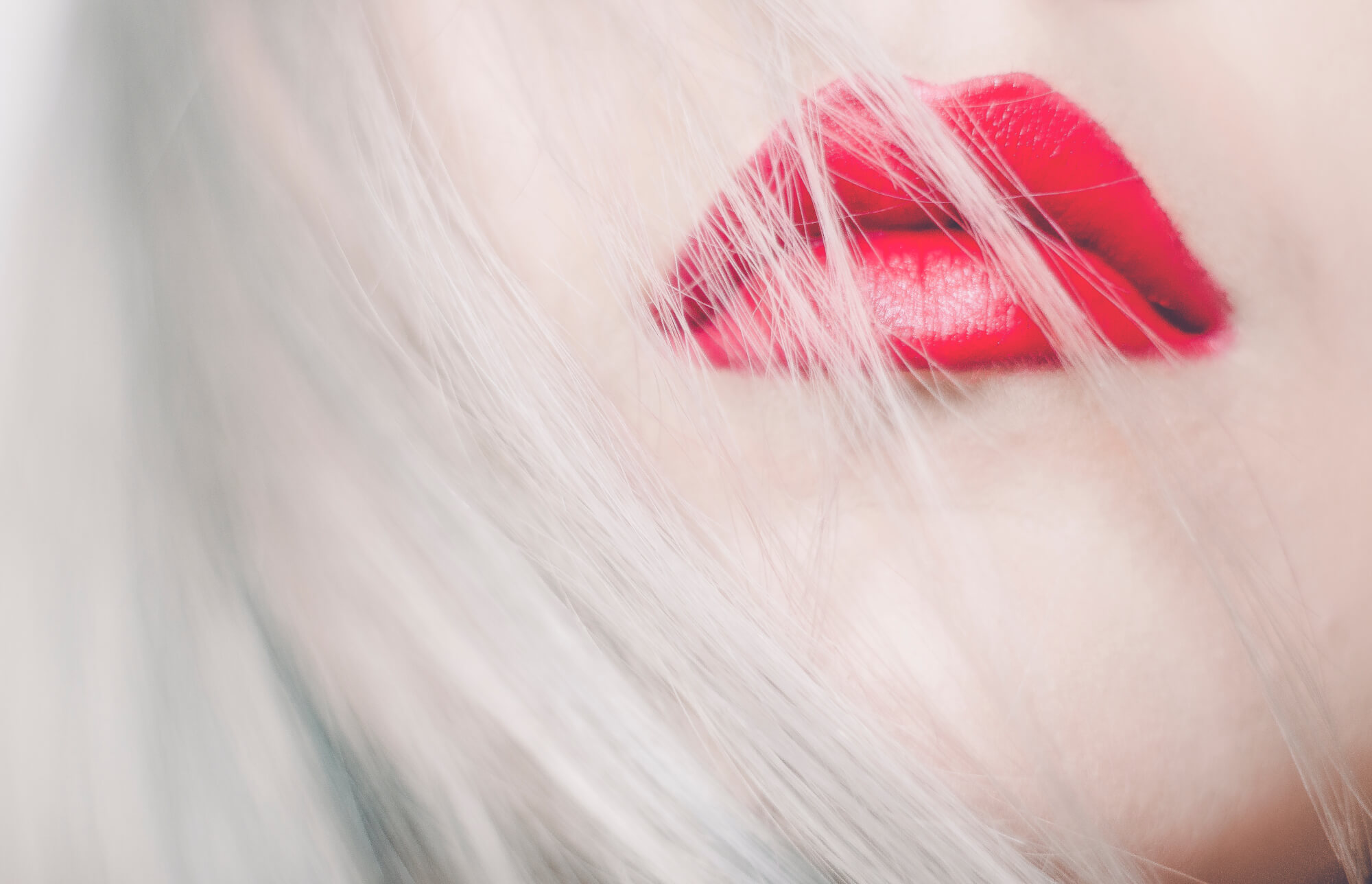 Close up of model's mouth with bright red lipstick on and blonde hair over their lips.