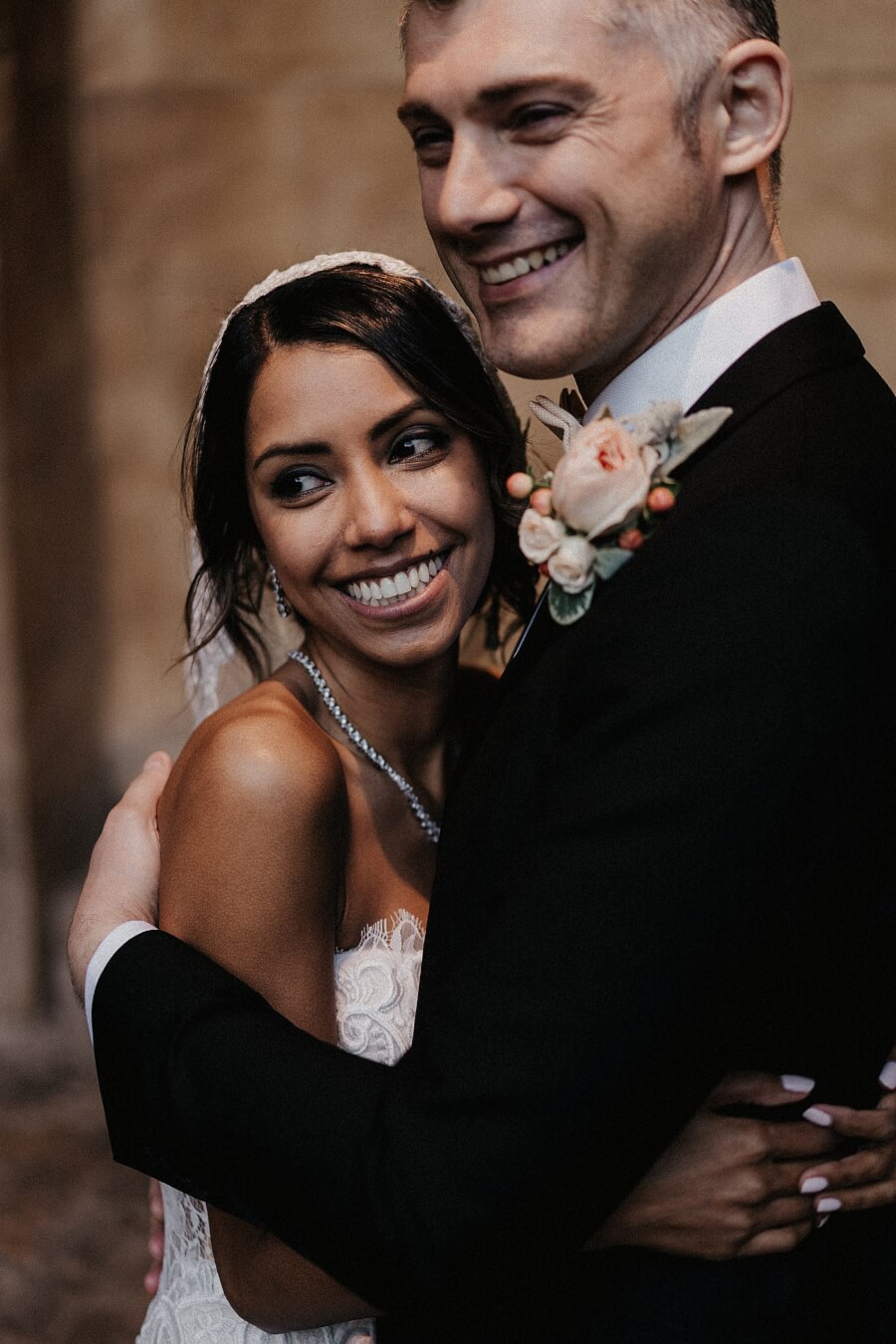 Bride and groom smiling whilst embracing and looking off camera. Bride's hair and makeup have been done by Bristol makeup artist Evie Smith.