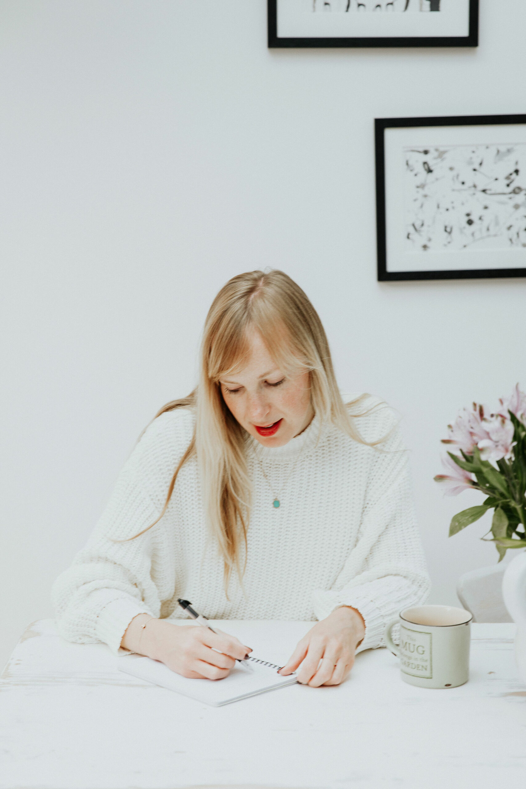 Evie, a makeup artist, wearing a white jumper,looking down as she writes in a notepad
