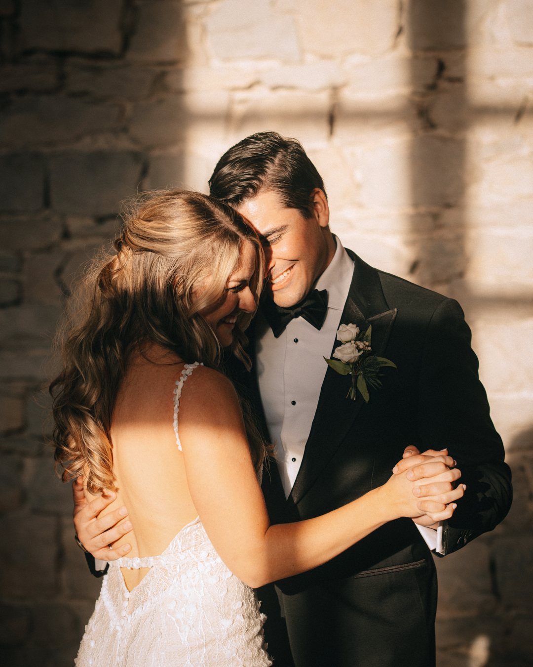 Bride and groom dancing and smiling in the sunlight.