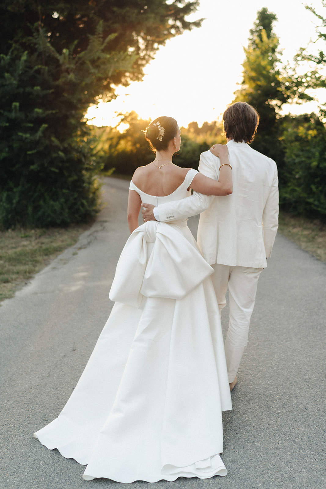 Bride and groom walk together down a path as the sun goes down in the background.