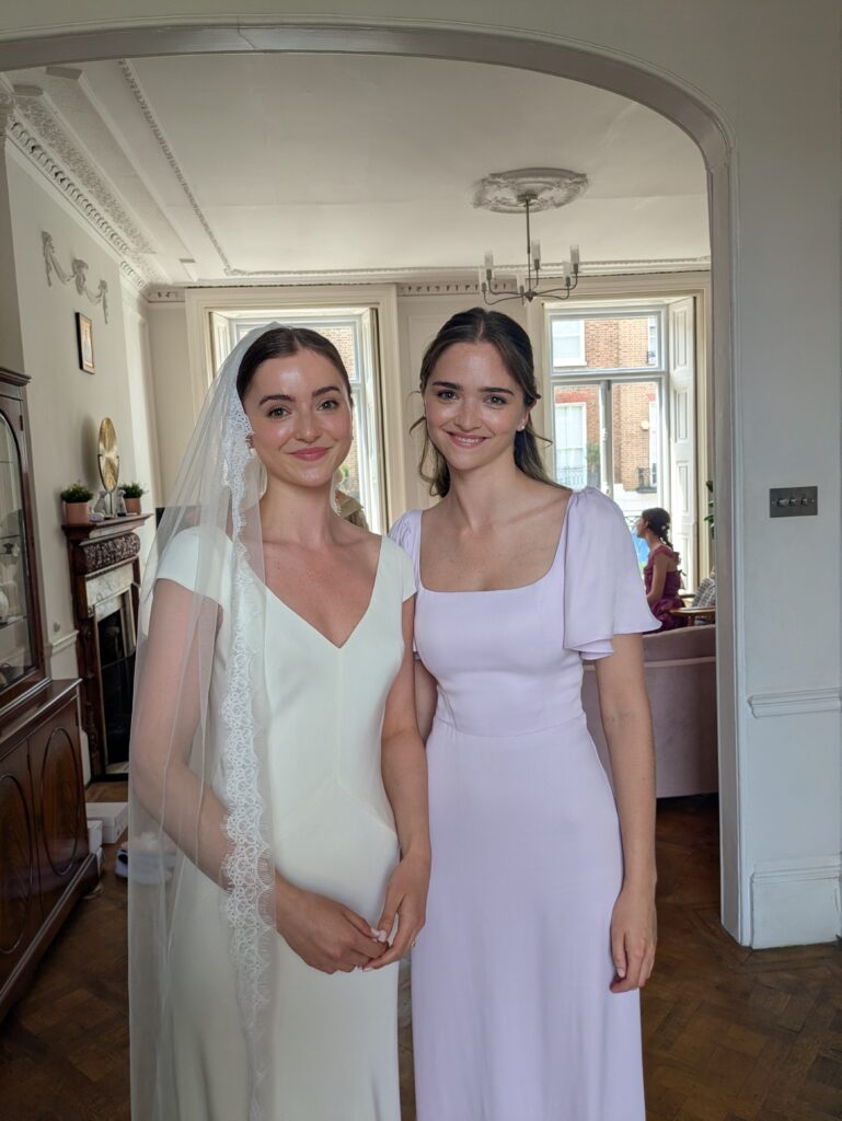 a bride and bridesmaid staring into the camera at a london wedding. the bride is wearing a veil and the bridesmaid is wearing lilac.